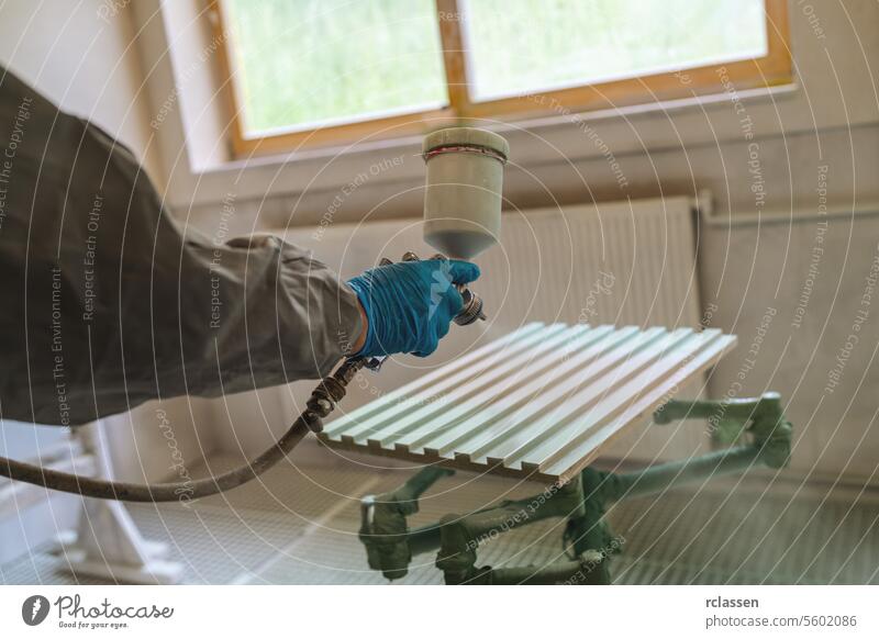 Person in protective clothing spray painting a bench with a window in the background carpenter craftsman mask spray gun painter wooden panel workshop