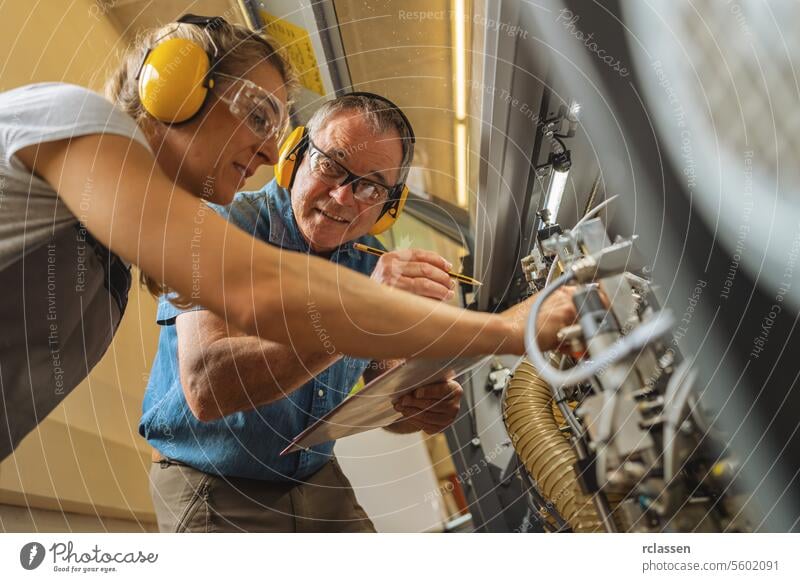 Technicians examining machinery with a clipboard and pen in a workshop professional craftsman carpentry technicians ear protection industrial teamwork