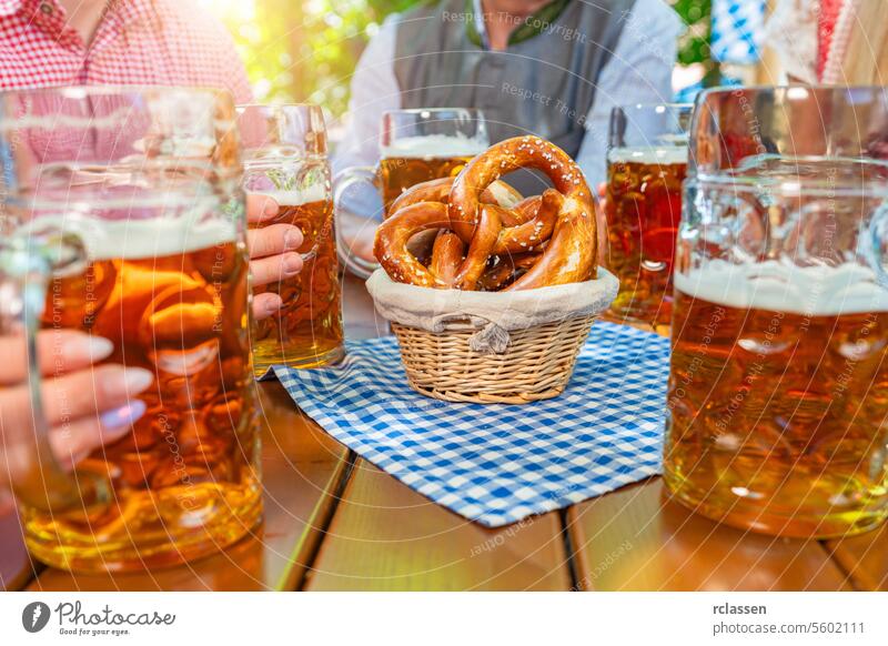 Group of happy friends drinking beer stein with brezen at Oktoberfest in bavaria german bavarian bar celebration cheers dirndl lager hangout toasting party pup