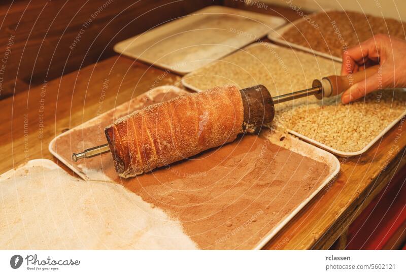 woman hand applies suggar on a trdelnik, kurtoscalacs or Baumstriezel on a Spiral rod in a Booth at christmas market munich december hungary bread store dessert