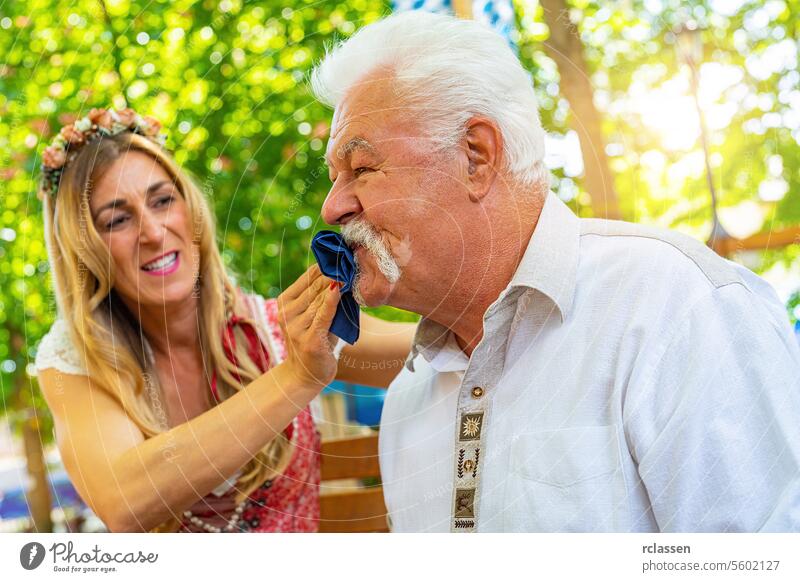 daughter looks angry and cleaning mouth with cloth from her grandfather r in Bavarian beer garden or oktoberfest dirty dementia pensioner bavarian flag old man