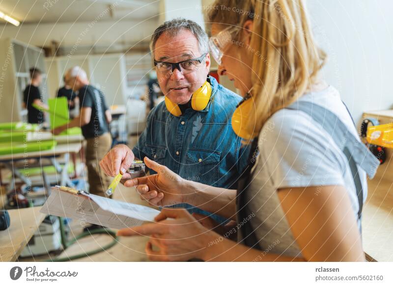 Instructor explaining measurements on blueprint to apprentice in a carpentry workshop professional craftsman teamwork workbench furniture industry worker