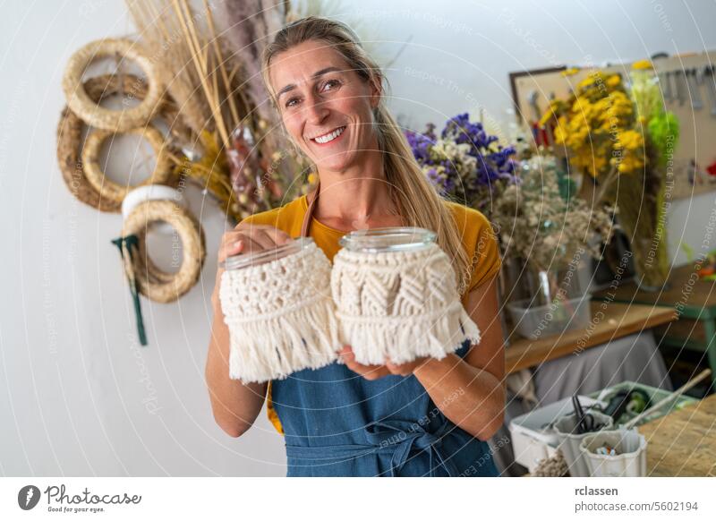 Joyful florist holding macrame decorated jars in her creative workshop joyful smiling woman crafting handmade diy macrame jars decoration happy art hobby design