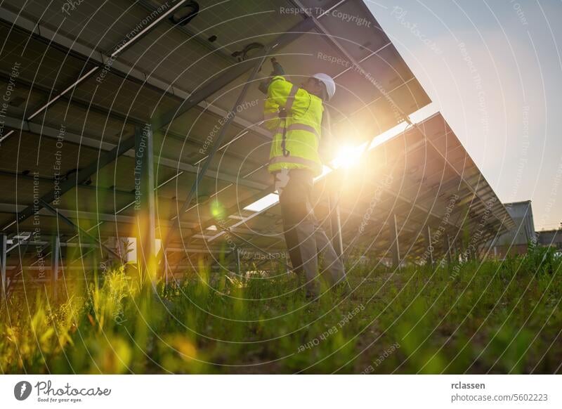 Technician assembling solar panels with a cordless drill at a solar field from behind. Alternative energy ecological concept image. master engineer