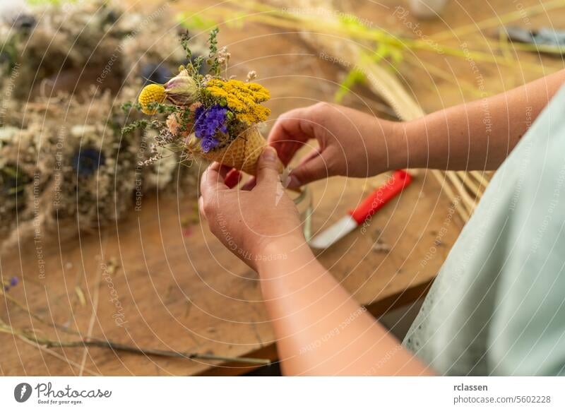 Hands crafting a small bouquet of colorful dried flowers in a cone, on a wooden table knife workshop hands floristry arrangement diy decoration handmade natural