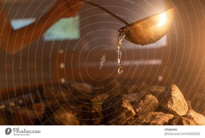 Woman pouring water onto hot stone in sauna room with a group of people. Steam an water on the stones, spa and wellness concept, relax in hot finnish sauna.