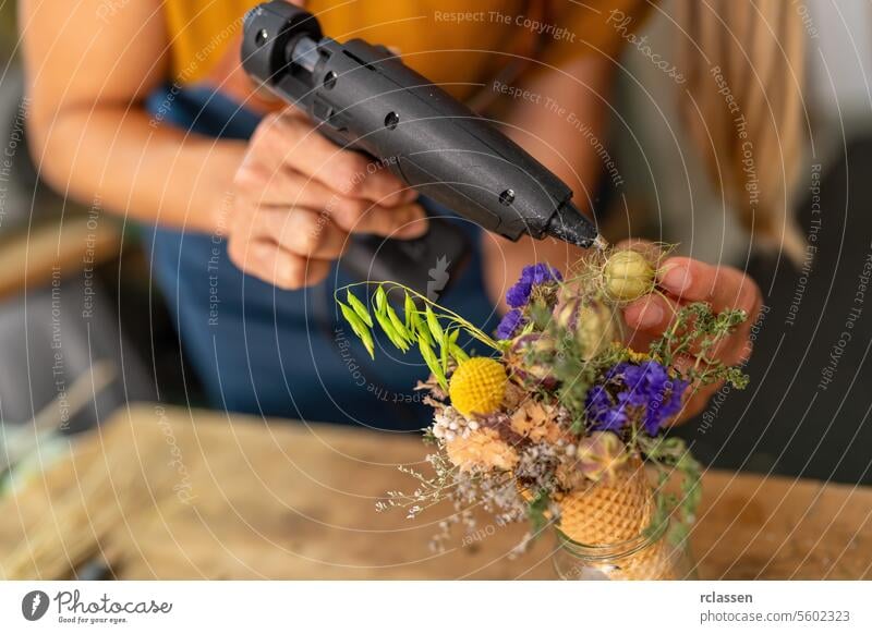 Close-up of hands using a glue gun to assemble a floral arrangement in a cone close-up diy flowers decoration workshop assembling creative hot glue design hobby