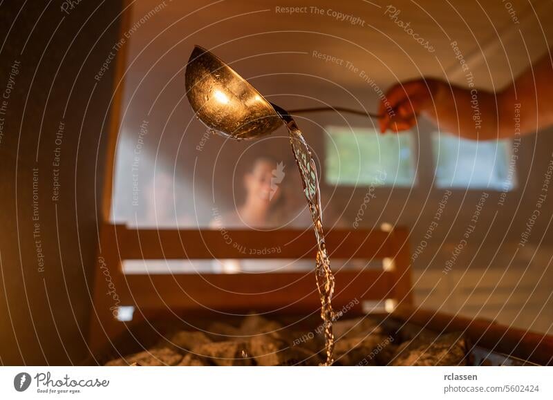 Man pouring water onto hot stone with metal spo in sauna room with a group of people. Steam an water on the stones, spa and wellness concept, relax in hot finnish sauna. Warm temperature bath therapy.