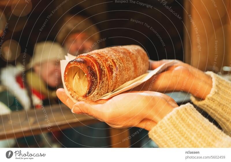 saleswoman holding Baumstriezel, trdelnik or kurtoscalacs in his heand in a Booth at christmas market couple beard old man december hungary bread store dessert