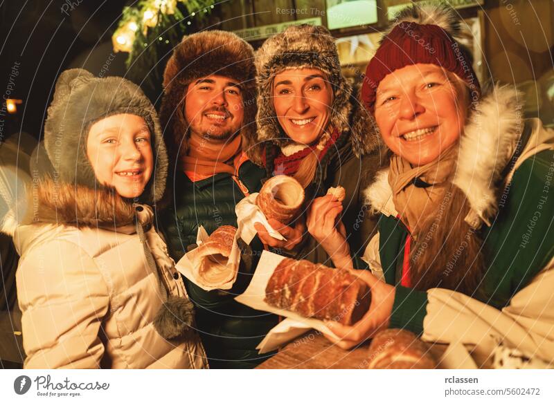 Happy family eating Baumstriezel or trdelnik in front of a Christmas Market in germany sweet snack sugar spiral baumstriezel kurtoscalacs grandmother daughter