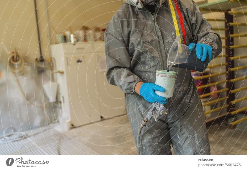 Painter in protective suit pouring blue paint into a spray gun container carpenter craftsman mask painter pouring paint protective gear gloves equipment