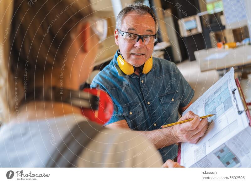 Carpentry instructor discussing blueprint details with an apprentice in a carpentry workshop teamwork professional craftsman workbench furniture industry worker