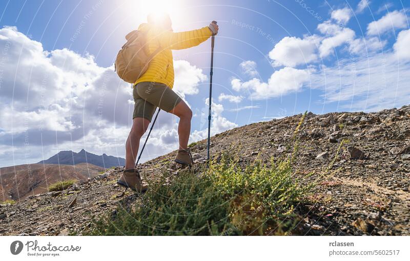 Hiker with backpack and trekking pole ascending a mountain trail under a cloudy sky fuerteventura hiker ascent hiking adventure outdoor wilderness