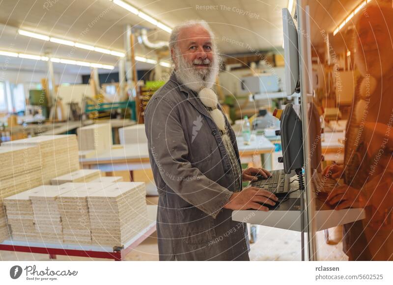 Smiling bearded man operating a a cutting machine computer in a carpentry workshop professional craftsman safety glasses operating computer woodworking