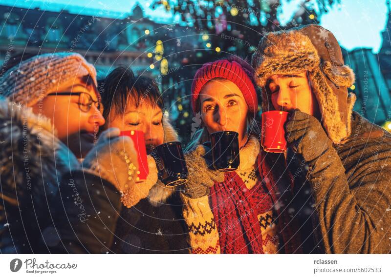 Happy friends having fun drinking mulled wine and hot chocolate at Christmas Marke punch merry christmas cup gloves traditional christmas market advent german