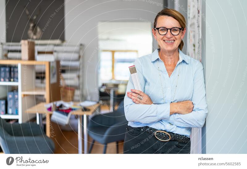 professional smiling tailor woman with hair Braid, wearing glasses and a blue striped shirt, stands in a modern workspace and holding a ruler. office scissors