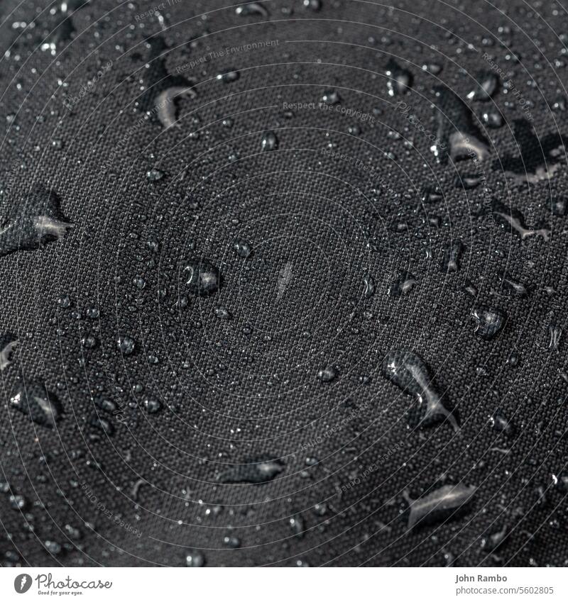 dark gray waterproof hydrophobic cloth closeup with water drops rain rough selective focus blur liquid fabric background texture wet weather surface clean dew