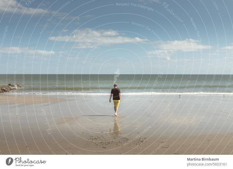 Caucasian man walking on the beach of Edisto Island, South Carolina caucasian vacation summer day edisto beach edisto island landscape travel wooden blue