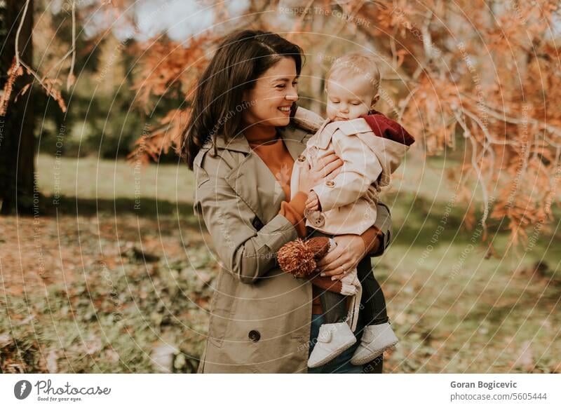 Young woman holding cute baby girl in the autumn park small caucasian mother outside daughter child little love happiness together family play mom smile season