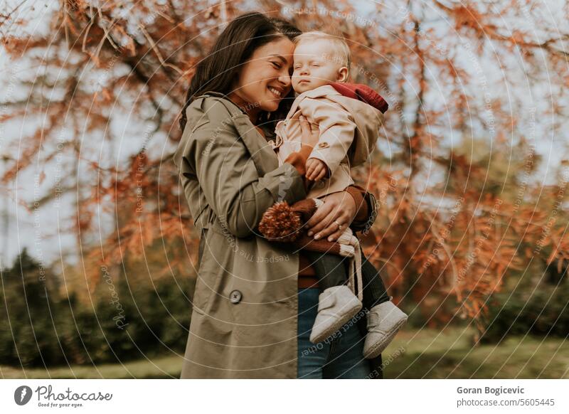 Young woman holding cute baby girl in the autumn park small caucasian mother outside daughter child little love happiness together family play mom smile season