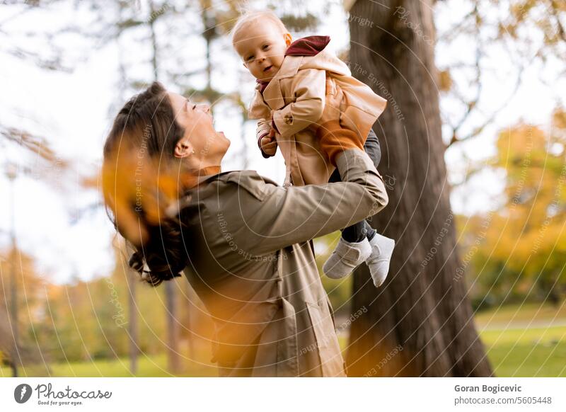 Young woman holding cute baby girl in the autumn park small caucasian mother outside daughter child little love happiness together family play mom smile season