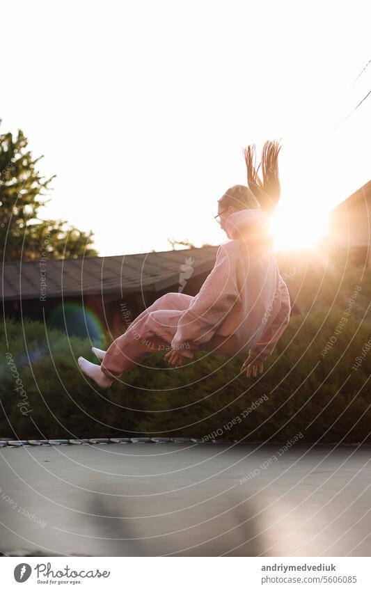 Happy little child girl having fun and jumps on trampoline outdoors, at backyard of the house on sunny summer day, active recreation on summertime vacation. Happy childhood concept. Children's day.