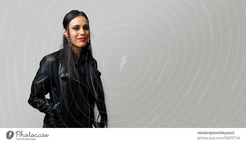 Portrait of a gothic rocker-looking woman, looking directly at the camera, wearing a leather jacket, on plain gray background female beauty person portrait