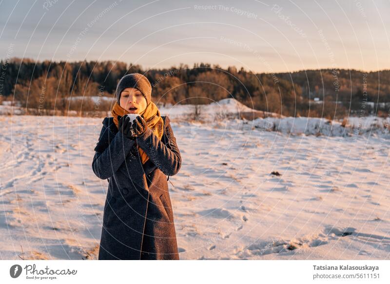 A woman in winter with a handful of snow in her palms prepared to blow it away warm clothes female people person European White adult mid adult hold one