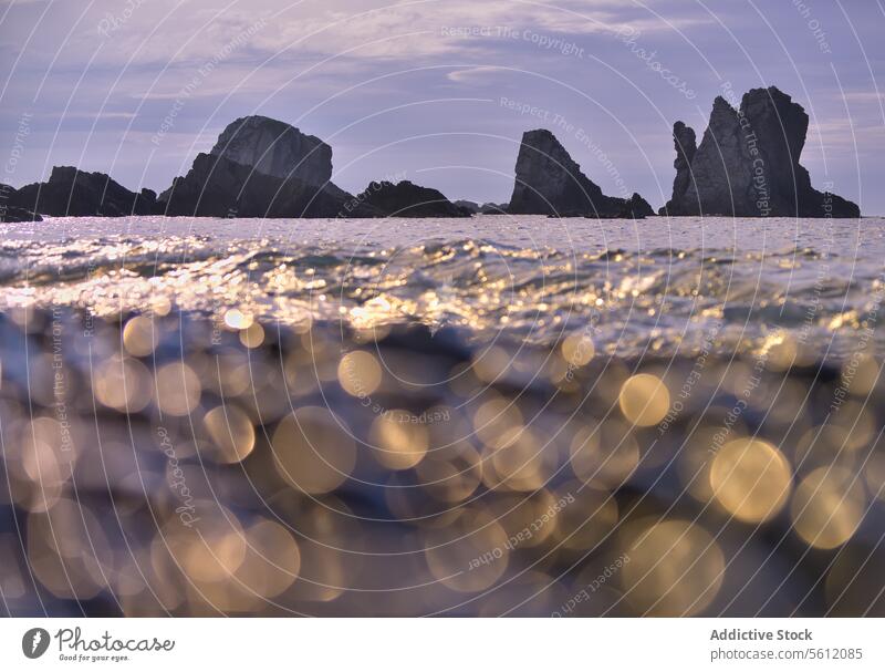 Sparkling ocean waves with rocky silhouette at dusk sparkle serene beauty majestic background soft sky nature landscape bokeh seascape water coast coastal