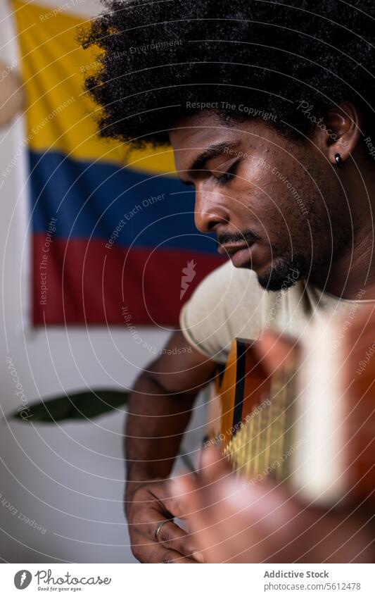 Serious man playing guitar at home young practice portrait colombian flag confident serious afro hair sit focus acoustic string instrument weekend closeup