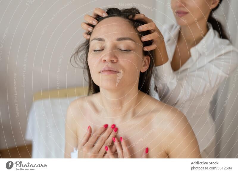 Crop hands of unrecognizable masseuse doing hair massage to topless female customer enjoying therapy with closed eyes in spa session head eyes closed crop sit