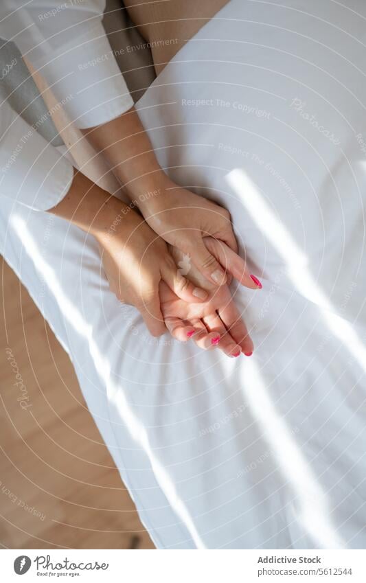 High angle crop anonymous therapist doing acupuncture massage on female client's hand on comfortable white bed in spa salon during session women high angle