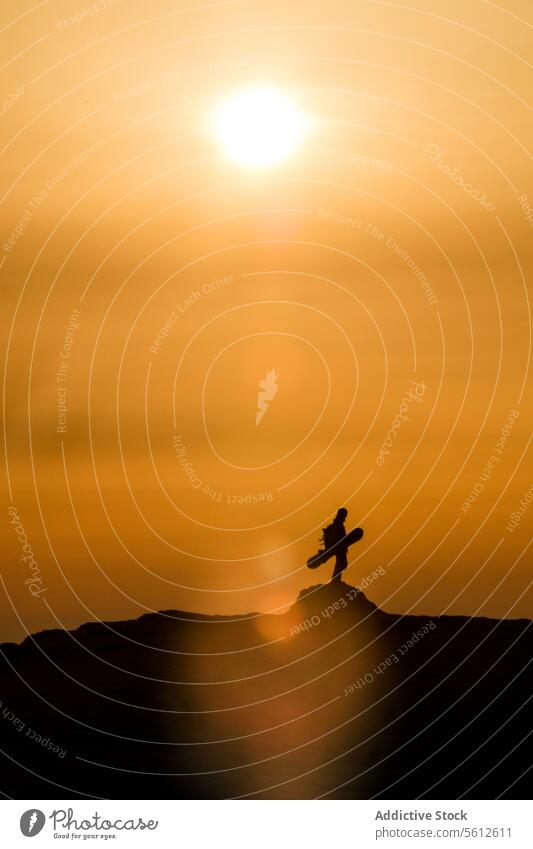 Full body of silhouette unrecognizable person with snowboard standing on top of mountain against sky with bright sun during sunset at Japan in winter vacation