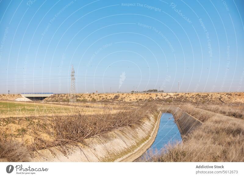 Canal in arid landscape with electricity pylon and highway dry barren canal irrigation water energy infrastructure transmission tower sky blue nature