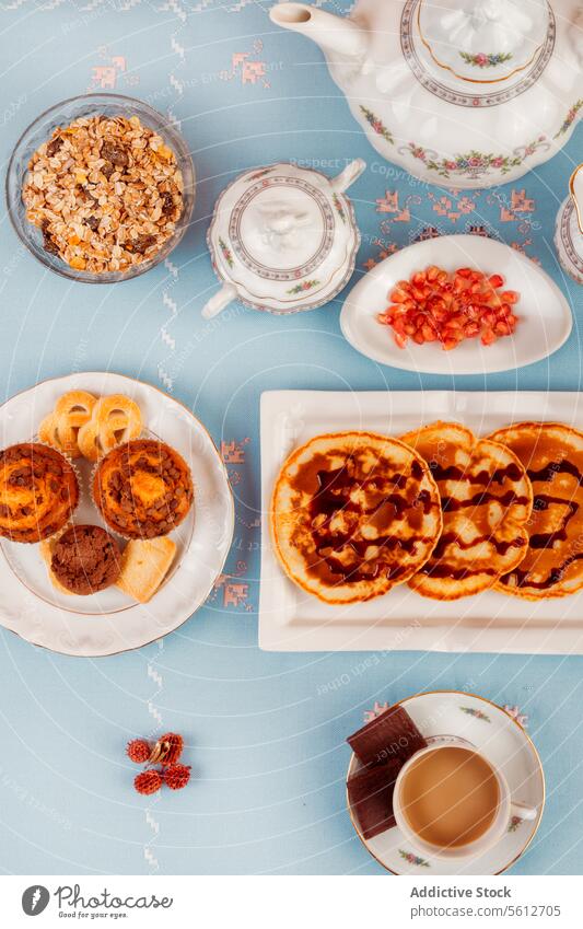 Elegant tea time layout with snacks and tea set elegant top-down view spread teapot cup background blue waffle tart granola pomegranate seed plate saucer spoon