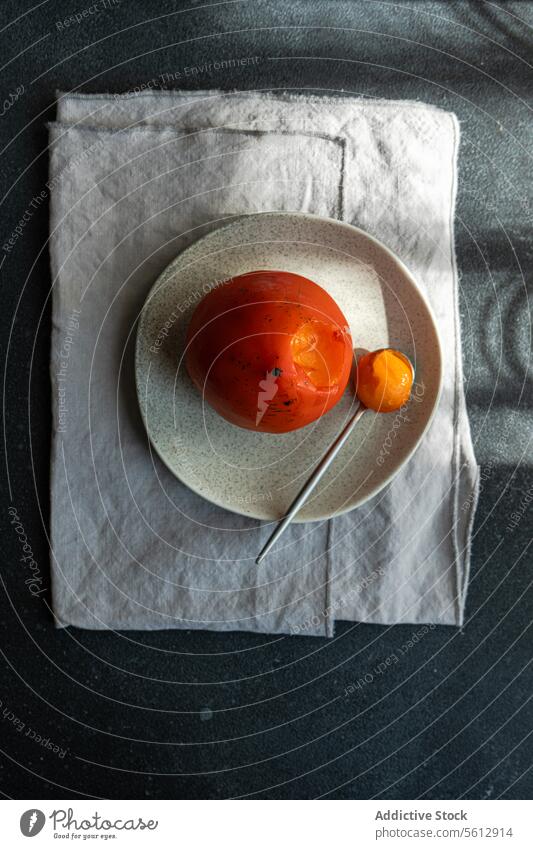 Gleaming Persimmon on Plate with Shadow Play persimmon plate spoon shadow ripe fruit dessert ceramic vibrant dramatic curve gleaming seasonal tabletop fabric