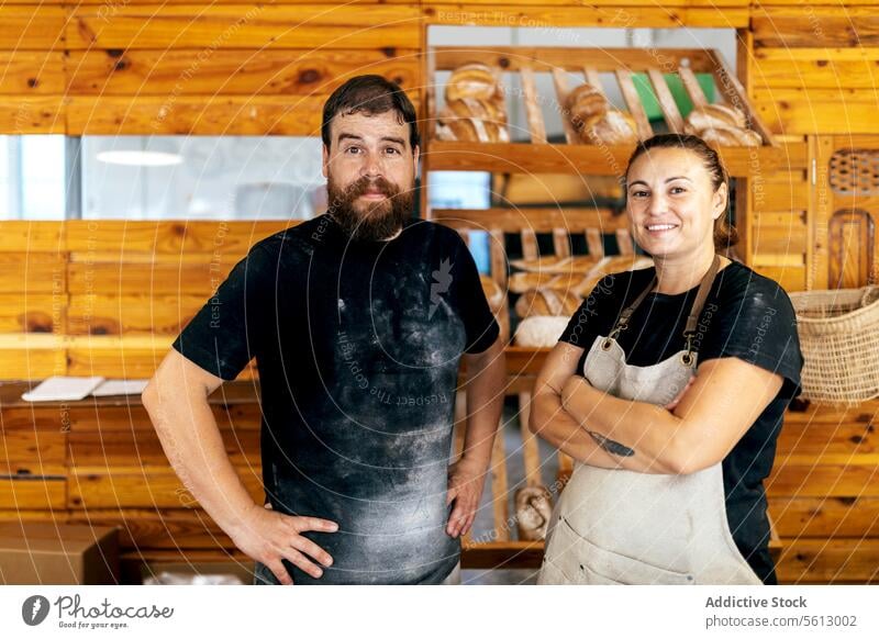 Confident sellers standing in bakery shop coworker bread baked positive colleague apron casual attire smile confident together teamwork looking at camera wooden