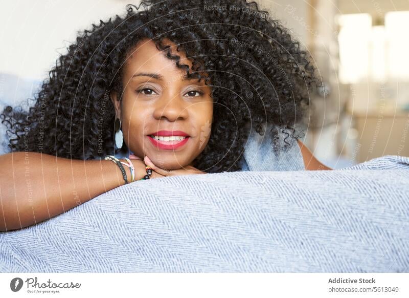 Female with curly hair on sofa woman beautiful lying closeup portrait afro hairstyle living room confident calm relax home couch attractive looking at camera