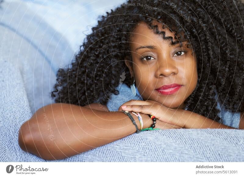 Female with curly hair on sofa woman beautiful lying closeup portrait afro hairstyle living room confident calm relax home couch attractive looking at camera