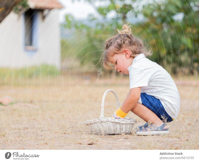 Side view of little boy looking in wicker basket while crouching in garden picking backyard gardening vacation cute childhood learning gardener full body glove