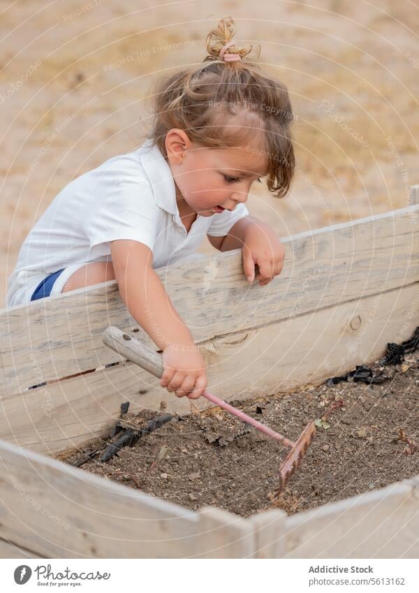 Side view of little boy using rake in raised garden bed at backyard soil planting vacation cute gardening holding playing lifestyle kid metal learning