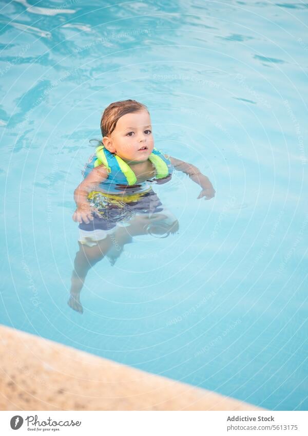 High angle of Cute boy wearing inflatable jacket while swimming in pool cute playful floating water child safety lifestyle recreation joy hobbies holiday resort