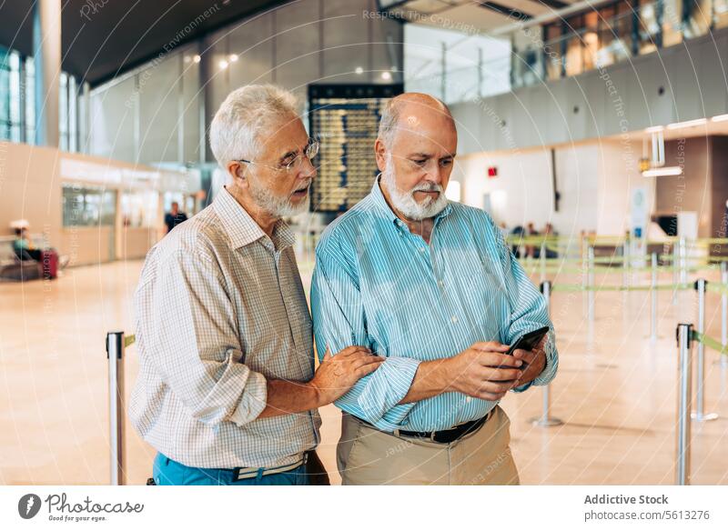 Aged travelers checking ticket at aerodrome passenger friends men board timetable wait departure airport beard phone passport stand serious boarding pass visa