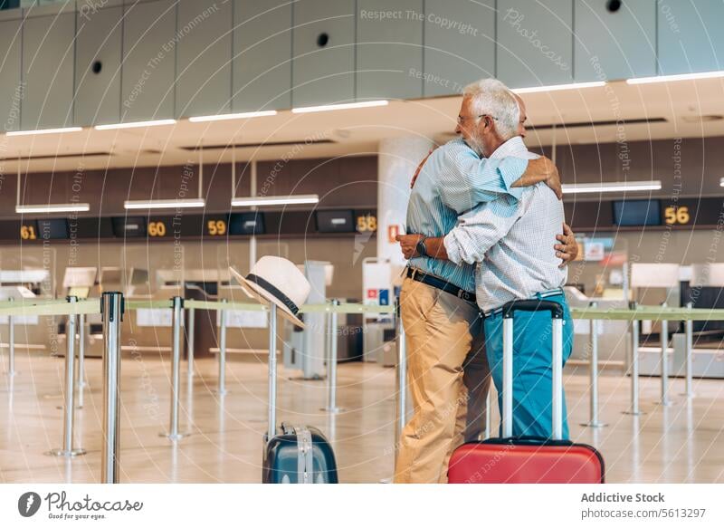 Senior travelers hugging at modern airport friends embrace happy luggage side view farewell aerodrome together stand suitcase casual attire separation departure