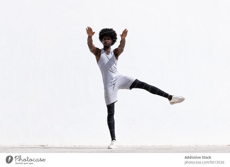 Serious black man stretching body over white wall athlete exercise afro hair arm confident focus balance effort sportsman serious leg stand street stamina