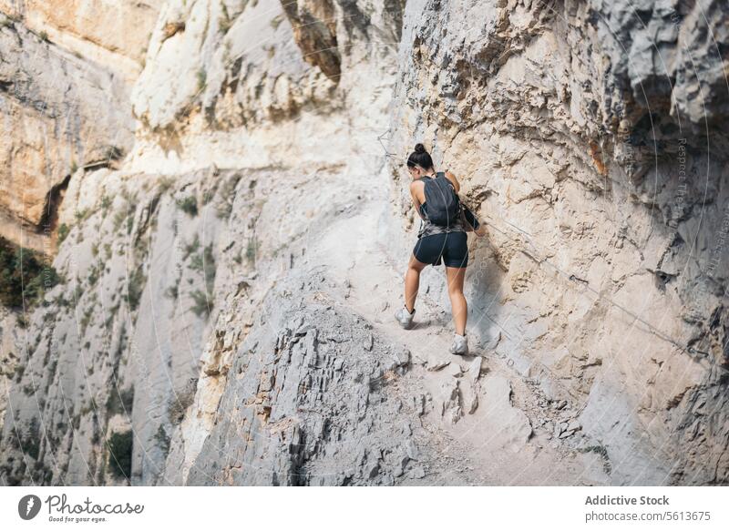 Back view full body of unrecognizable female hiker with backpack holding rope and trekking on majestic rocky mountain during weekend vacation nature risky