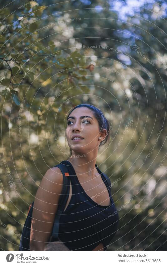 Serene woman looking away while hiking in forest traveler hike trekking calm backpack casual attire beautiful lifestyle tree positive looking over shoulder