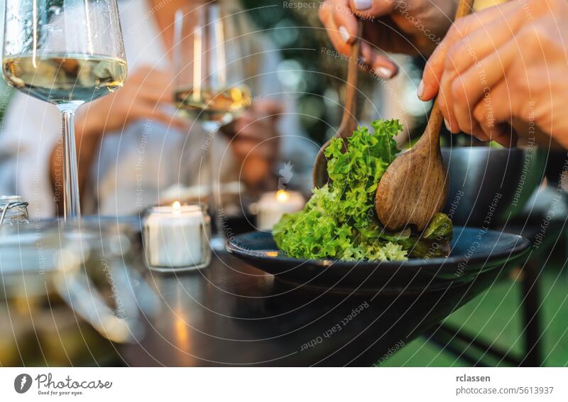 Close-up of salad being served with wooden utensils, with wine glasses and candles in background serving close-up healthy eating fresh gourmet dining meal