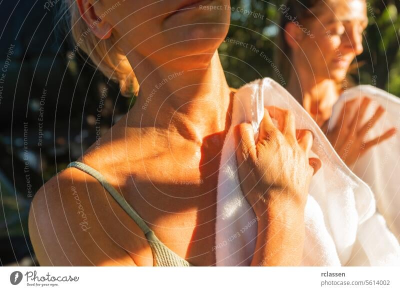 Close-up of two women drying off with towels in the sunlight after finnish sauna close-up spa wellness relaxation leisure skin care sunlit health luxury comfort