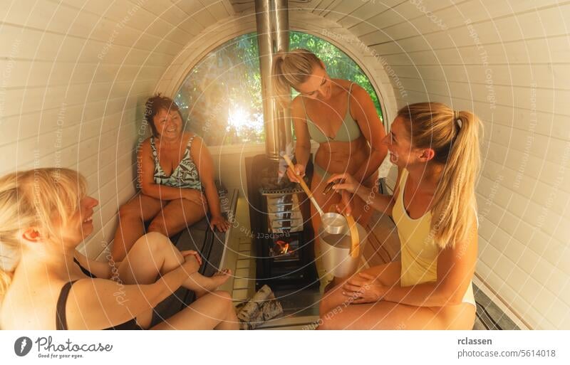 Four women in a sauna, one dripping sauna scent into a ladle of water over the heater. Mobile finnish sauna concept image aroma essence spa therapy self-care